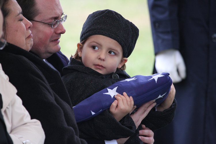 The granddaughter of Major Timothy D. Fulton clutches a folded American flag which was just given to her as she looks at her tearful mother during memorial services for her grandfather, Major Fulton at Arlington National Cemetery. © Mike Lynaugh