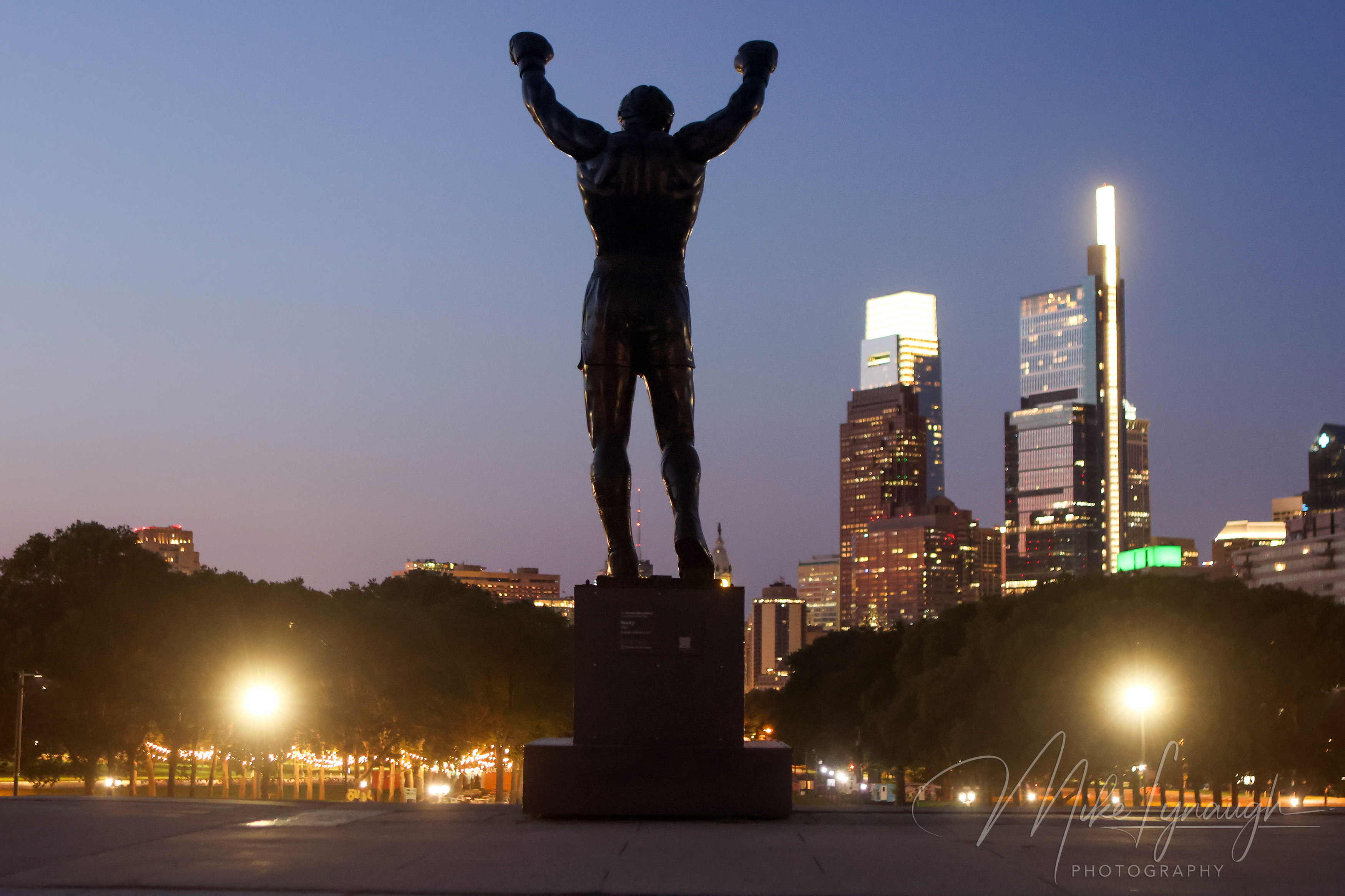 Rocky Statue — Overlooking the Skyline at night. The Rocky statue photographed at the start of sunrise as it overlooks the Philadelphia skyline from the top of the Rocky Steps.
