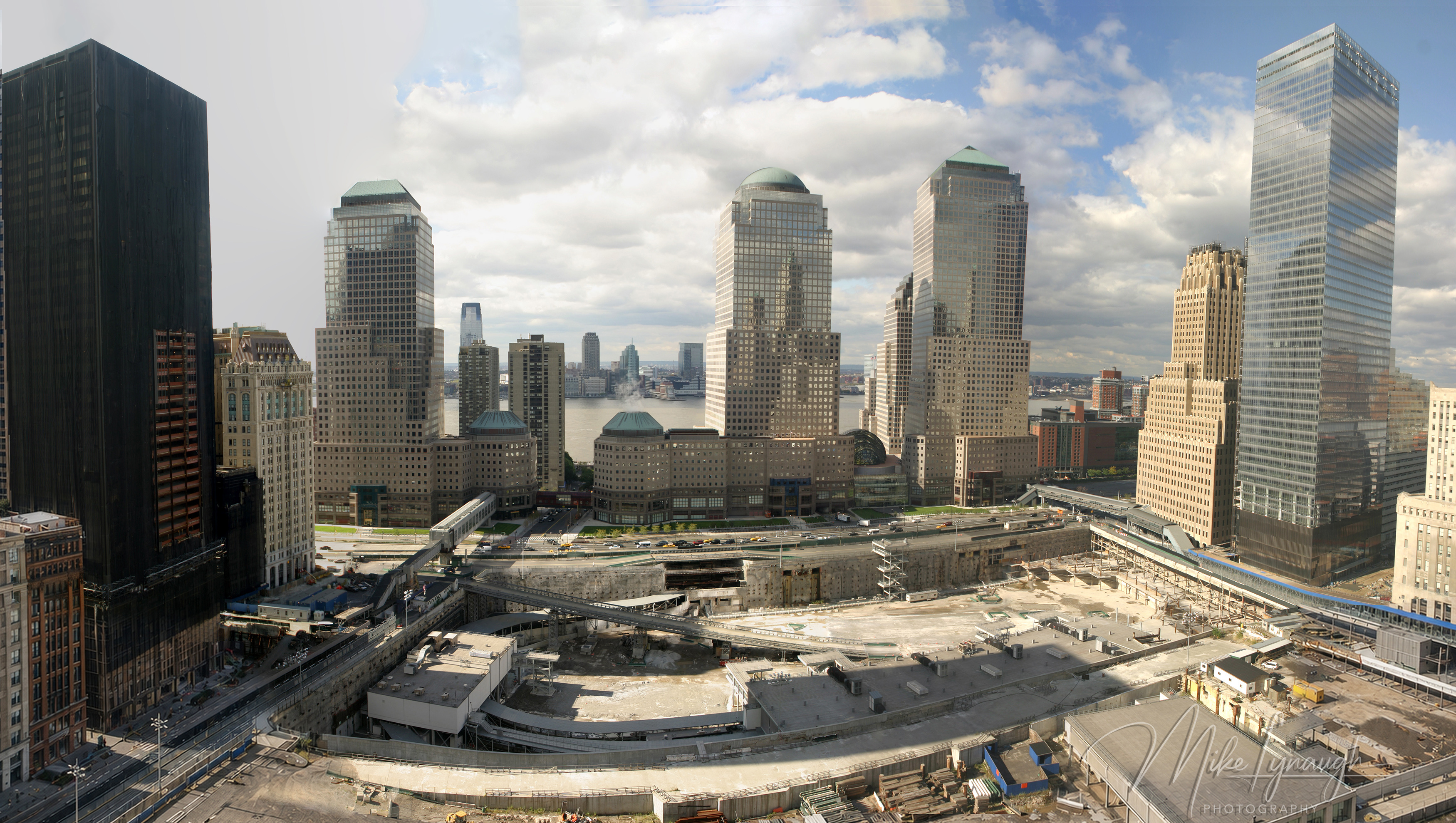 A wide panoramic photograph taken from a 20th-floor WTC Family Room window at One Liberty Plaza, looking down into the Ground Zero site toward the Hudson River in October 2008.