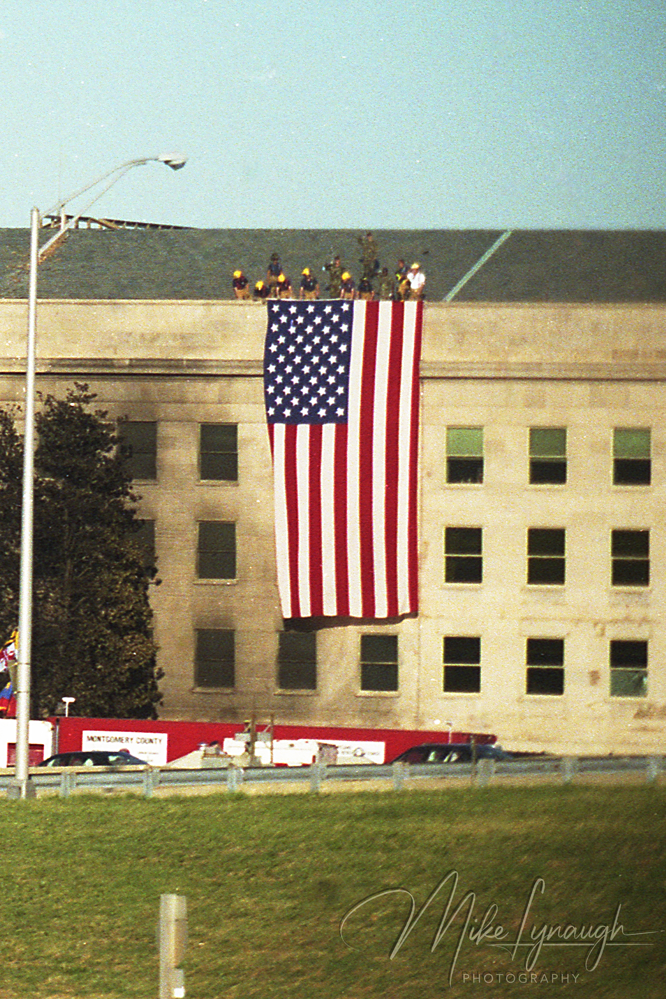 Vertical close-up of a large American flag hanging down the outer wall of the Pentagon with personnel on the roof on September 12 2001