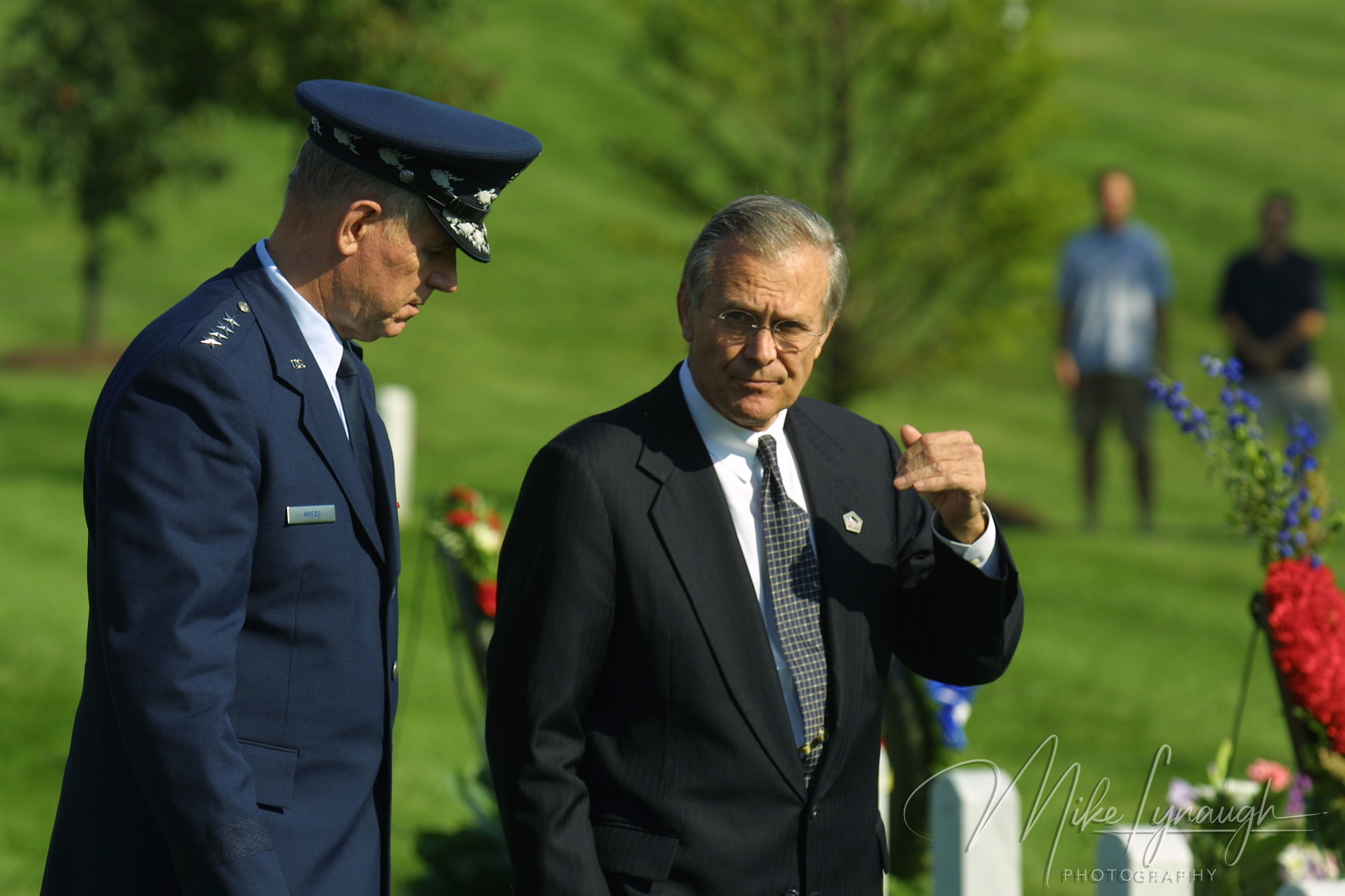 A medium close-up of Secretary of Defense Donald Rumsfeld gesturing with his hand while standing alongside Air Force General Richard Myers at Arlington National Cemetery
