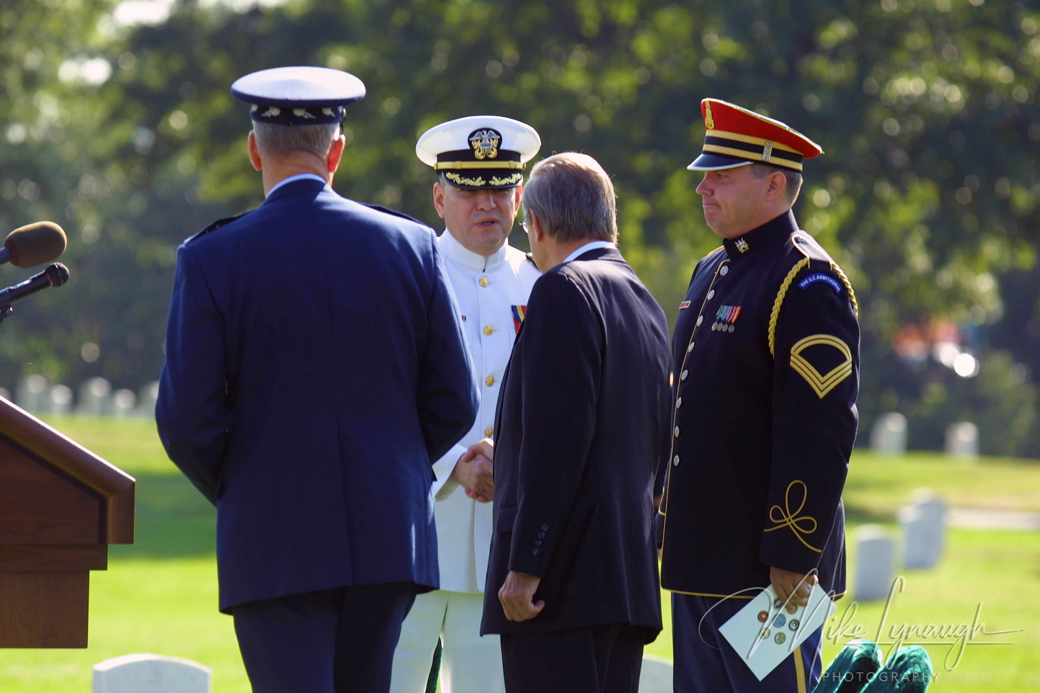 Secretary of Defense Donald Rumsfeld shaking hands with a Navy chaplain in a white dress uniform next to General Richard Myers and an Army vocalist at Arlington National Cemetery