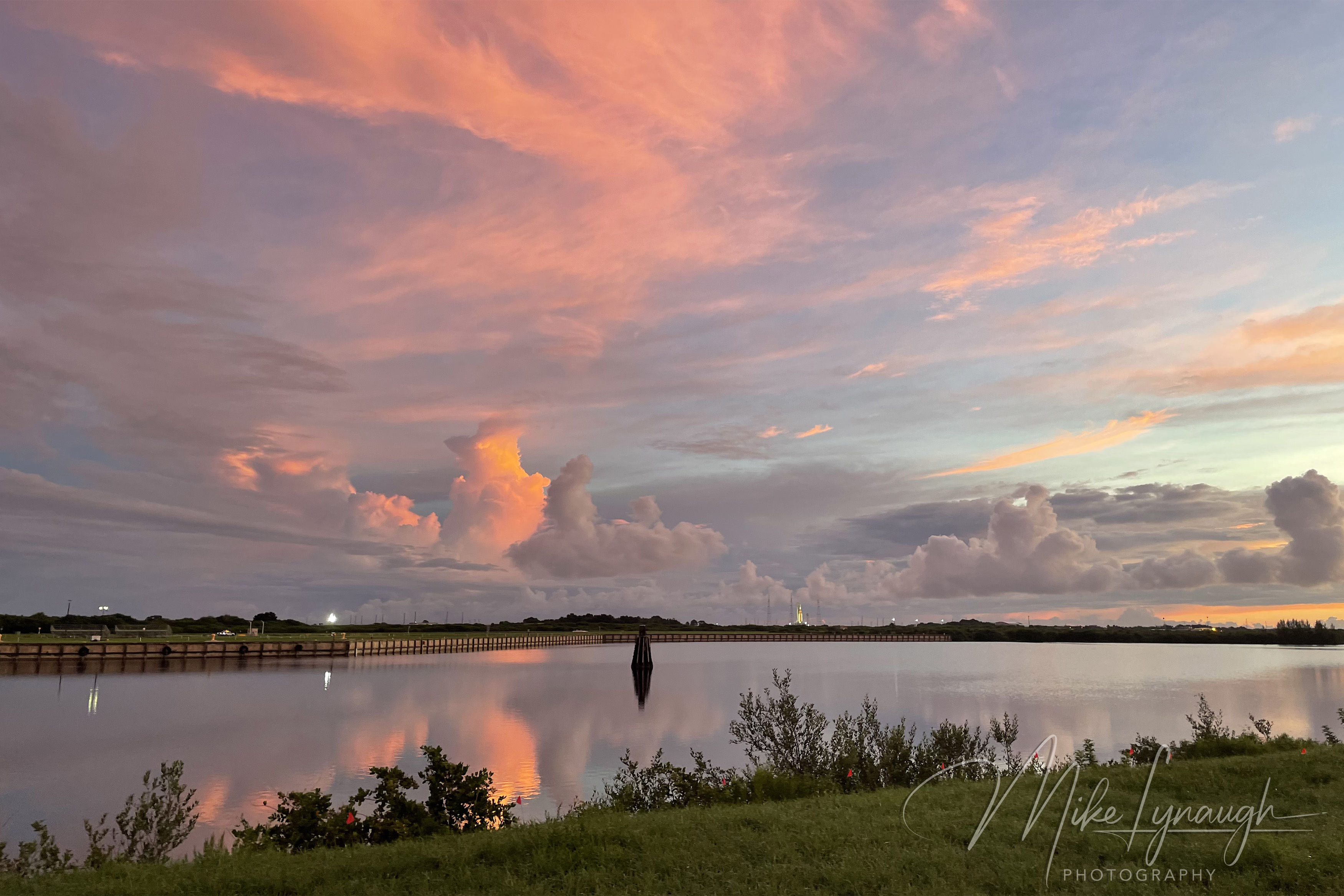 A wide landscape photograph capturing vibrant coral and peach sunrise clouds reflecting across the glassy Turning Basin.